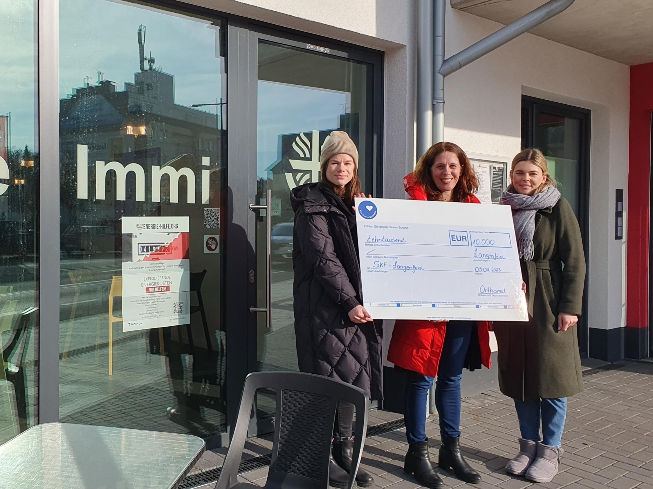 Kim Horeis (links) und Lisa Trapp (rechts), Mitarbeiterinnen von Orthomol, übergeben einen Spendenscheck an Stephanie Krone, Geschäftsführerin des SkF e.V. Langenfeld.